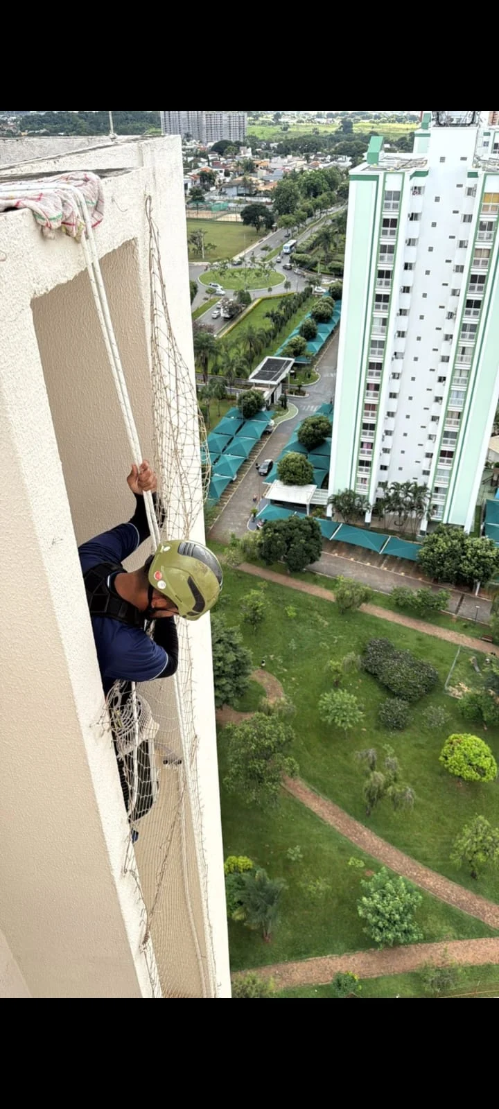 Profissional da Eletrogelo com capacete e equipamentos de acesso por corda na fachada de um prédio